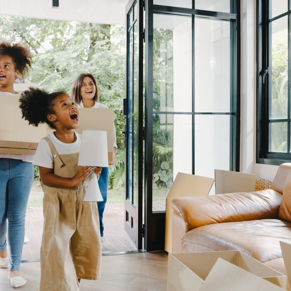 Happy African American young family bought new house. Mom, Dad, and child smiling happy hold cardboard boxes for move object walking into big modern home. New real estate dwelling, loan and mortgage.